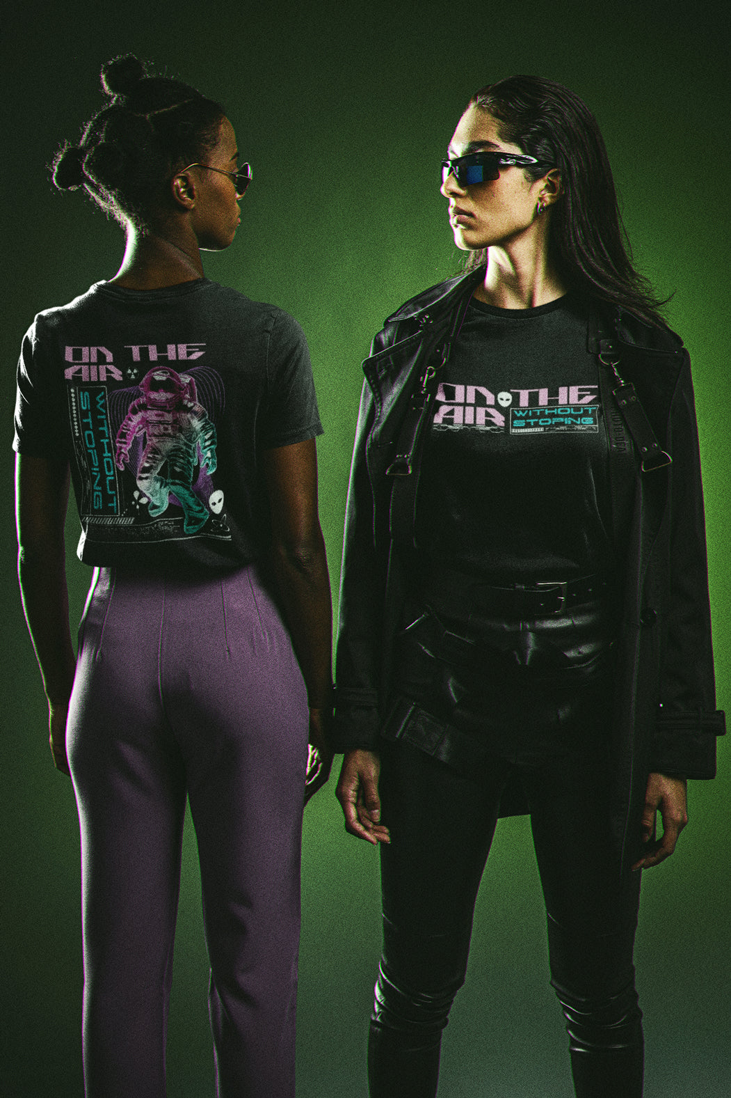 Two women wearing black t-shirts with graphic designs on a green background